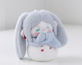 May include: A plush doll with light blue hair and long ears, wearing a light blue knit scarf. The doll has a white rounded body with small red spots, embroidered teal eyes, and pink cheeks. A small red bead earring is visible on the left side.