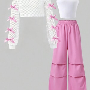 Op de afbeelding: Een driedelige outfit bestaande uit een wit off-shoulder visnettop met lange mouwen en kleine roze strikjes op de mouwen, een wit mouwloos crop-top hemdje en een wijde roze broek met horizontale, gelaagde panelen over de broekspijpen.