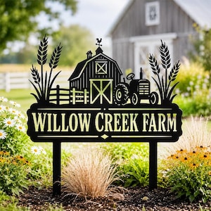 May include: A black metal garden sign featuring a silhouette of a barn, a tractor, and wheat stalks. The text "WILLOW CREEK FARM" is cut out in a light yellow color. The sign is supported by two vertical stakes extending from the bottom edge.