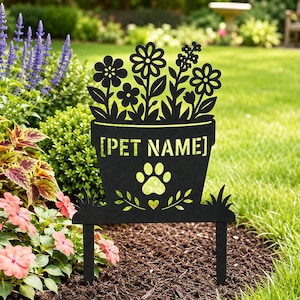 May include: A black metal garden stake featuring a silhouette of a flower pot filled with various flowers. The pot displays the text [PET NAME] in a stencil font, positioned above a paw print and a small heart, supported by two ground spikes.