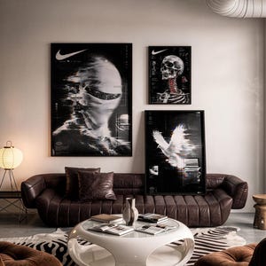 May include: A living room featuring a brown tufted leather sofa, a white circular coffee table with open sides, and three framed posters on the wall. The posters display a Nike logo, a human skull, and a white bird with digital glitch effects.