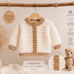 Puede incluir: Una chaqueta de ganchillo de manga larga para bebé de 4 meses, con cuerpo en color blanco roto y ribetes en color tostado en el cuello, puños y bajo. El cierre frontal tiene siete botones tostados. Una etiqueta circular dice Handmade with love.