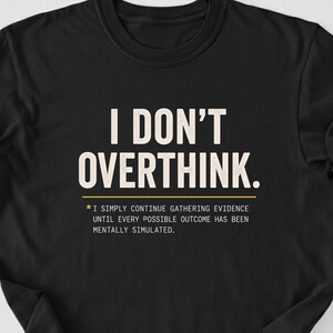 May include: A black short-sleeved t-shirt featuring the white text I DON'T OVERTHINK. followed by a yellow asterisk and the smaller white text I SIMPLY CONTINUE GATHERING EVIDENCE UNTIL EVERY POSSIBLE OUTCOME HAS BEEN MENTALLY SIMULATED.