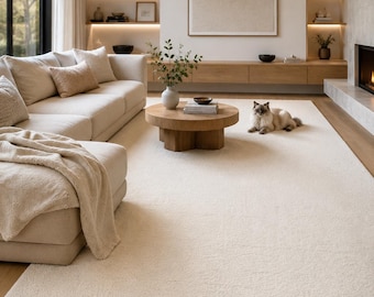 May include: A large, rectangular, cream-colored area rug with a thick, textured pile. The rug features a soft, plush surface that covers the floor space in a living room, extending from the base of a light-colored sofa to a fireplace hearth.