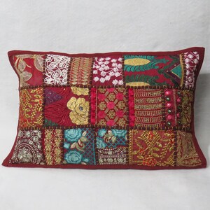 Op de afbeelding: Een rechthoekig sierkussen met een patchworkontwerp van verschillende stoffen vierkanten. De stof bevat tinten rood, goud, talingblauw en wit met ingewikkeld borduurwerk, metallic draaddetails, bloemmotieven en kleine kraalaccenten.