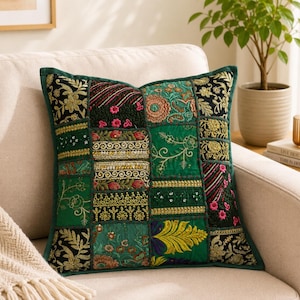 Peut inclure: Un coussin décoratif carré présentant un motif patchwork composé de divers panneaux de tissu vert et noir. La surface est ornée de broderies florales complexes dorées, roses et orange, d'accents en fil métallique et de perles détaillées.