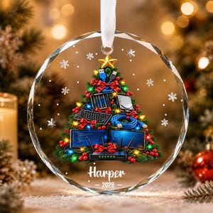 May include: A circular glass ornament featuring a Christmas tree decorated with computer hardware including a keyboard, monitors, cables, and a router. The tree is adorned with red bows, lights, and a gold star. The name Harper and 2026 are printed below.