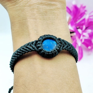 Peut inclure: Un bracelet macramé noir avec une pierre ronde bleu vif au centre. Le bracelet est tissé de manière complexe avec un motif détaillé, mettant en valeur le savoir-faire. Le bracelet est conçu pour être porté au poignet.