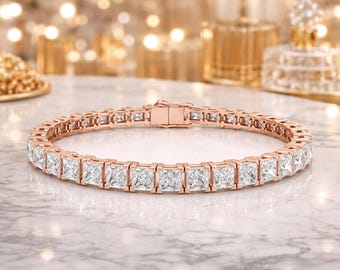 Op de afbeelding: Een roségouden tennisarmband met een doorlopende rij vierkant geslepen, heldere stenen in een zetting met pootjes. De armband is voorzien van een veilige baksluiting en toont een uniform ontwerp van geschakelde metalen segmenten en stenen.