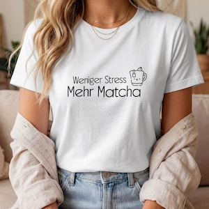 Könnte beinhalten: Weißes T-Shirt mit dem deutschen Text "Weniger Stress Mehr Matcha" und einer schwarzen Teetassen-Illustration. Das T-Shirt hat einen Rundhalsausschnitt.
