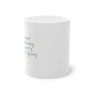 Könnte beinhalten: Weißer Keramikbecher mit dem handgeschriebenen Text "your money marry me funny" in Türkis. Der Becher ist zylindrisch und hat eine glänzende Oberfläche, geeignet für heiße oder kalte Getränke.