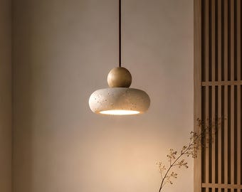 Pode incluir: Uma moderna luminária pendente com uma sombra clara e texturizada e uma esfera de madeira acima. A luz pende de um cabo escuro. Um vaso e uma tigela estão sobre uma mesa de madeira.