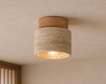 May include: A cylindrical ceiling light fixture with a natural stone shade and a wooden top. The light has a warm, inviting glow, and the fixture is mounted on a neutral-colored ceiling. The design is modern and minimalist.