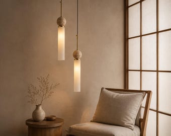 May include: Two pendant lights featuring cylindrical frosted glass shades suspended by thin black cords. Each light includes a spherical light-colored wood accent piece connected to a metallic rod, emitting a soft, warm glow from within the glass.