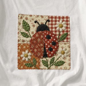 May include: A white short-sleeved t-shirt featuring a square fabric patch on the chest. The patch displays a ladybug surrounded by white daisies and green leaves, set against a background of four different patterned fabric squares in red and cream.