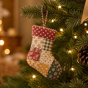 May include: A small fabric Christmas stocking ornament featuring a patchwork design of various floral and checkered patterns in red, green, white, and yellow. The cuff is red with white polka dots, and it hangs from a red and white twisted cord.