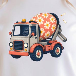 May include: A white t-shirt featuring a graphic illustration of a cement mixer truck. The truck has a light gray cab, orange fenders, and black tires. The mixing drum is coral-colored with a repeating white daisy flower pattern.