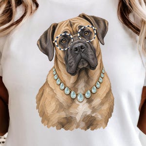 May include: A white t-shirt featuring a graphic illustration of a tan dog with a black muzzle. The dog is wearing round glasses with a blue and white chequered pattern and a gold-toned necklace with light blue, teardrop-shaped gemstones.