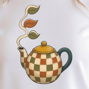 Könnte beinhalten: Ein weißes T-Shirt mit einer Grafik einer runden Teekanne mit Karomuster in Olivgrün und gebranntem Orange. Die Teekanne hat einen gelben Deckel, einen dunkelblauen Griff und einen Stängel mit drei Blättern, die aus dem Ausguss ragen.