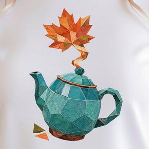 May include: A white t-shirt featuring a graphic print of a geometric, faceted teal teapot. A stylized orange and yellow maple leaf rises from the lid like steam. Two small, separate geometric triangles in orange and green sit below the teapot.