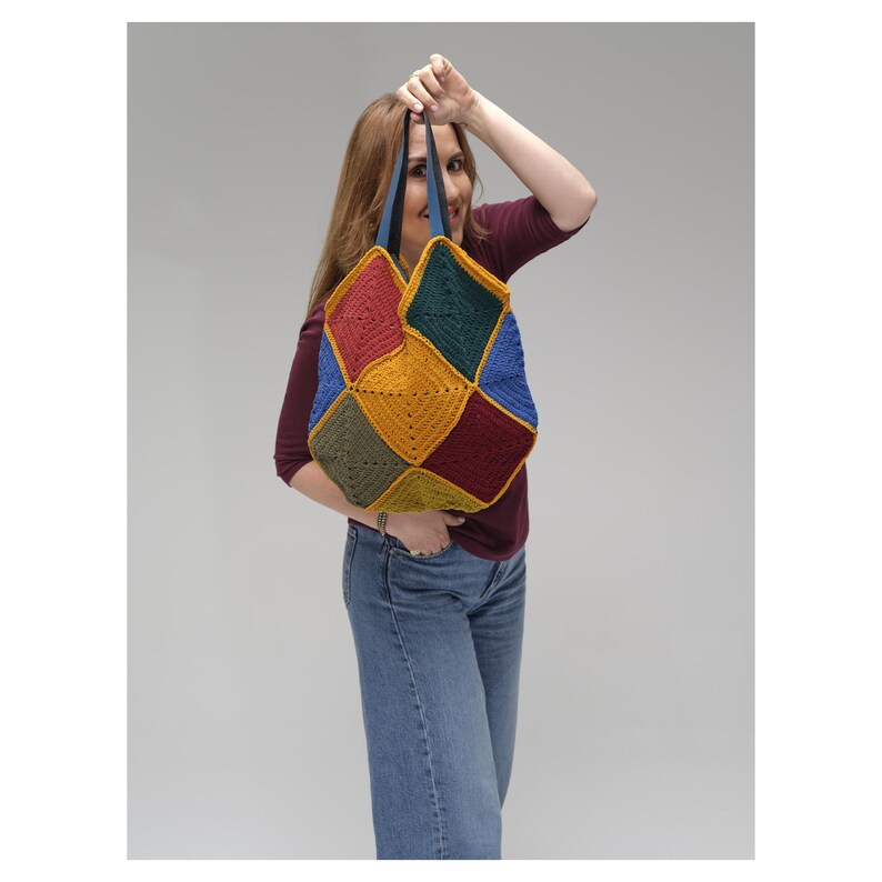 Puede incluir: Un bolso tote de ganchillo hecho a mano y colorido. El bolso presenta un dise&ntilde;o de patchwork con paneles en forma de diamante en varios colores, incluyendo rojo, verde, amarillo y azul. Tiene correas azules y lo sostiene una persona.