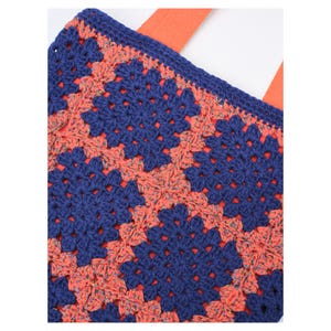 May include: A crocheted tote bag with a granny square pattern in navy blue and coral. The bag has orange straps and a matching navy blue border. The crochet work is detailed, showcasing the texture and design of the bag.