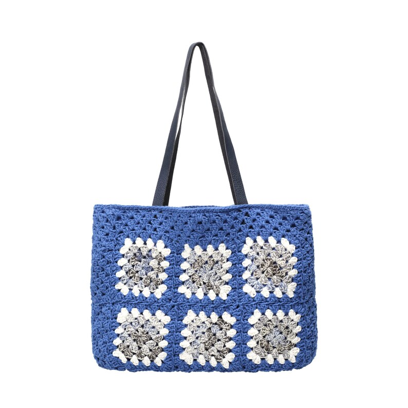Puede incluir: Un bolso tote rectangular de ganchillo con una base de hilo azul vibrante y seis motivos cuadrados. Cada motivo presenta un centro de hilo gris y blanco matizado rodeado por un borde blanco. El bolso incluye dos asas largas de color azul oscuro.