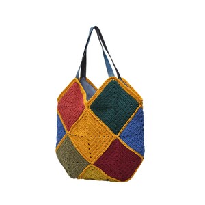 Puede incluir: Un bolso tote de ganchillo hecho a mano y colorido. El bolso presenta un dise&ntilde;o de patchwork con cuadrados rojos, azules, verdes, amarillos y verde oliva. Tiene un interior azul y correas negras y azules. Un accesorio &uacute;nico y elegante.