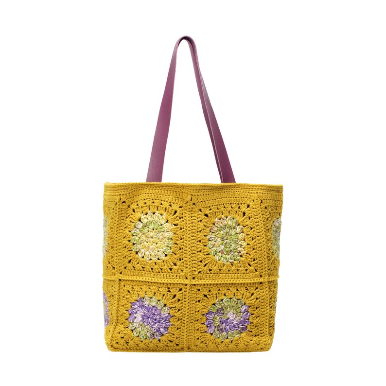 Puede incluir: Bolso tote de crochet amarillo mostaza con un estampado floral. El bolso tiene un asa de cuero morado. El dise&ntilde;o de crochet incorpora acentos verdes y morados dentro de los cuadrados florales. Un accesorio elegante y funcional.