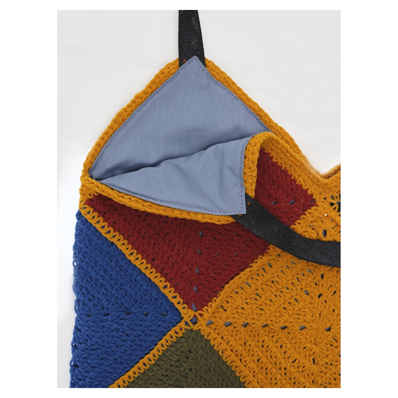 Puede incluir: Un bolso tote de ganchillo hecho a mano y colorido. El bolso presenta un dise&ntilde;o de patchwork con cuadrados azules, rojos, verde oliva y amarillo mostaza. El interior est&aacute; forrado con tela azul claro y tiene asas negras.