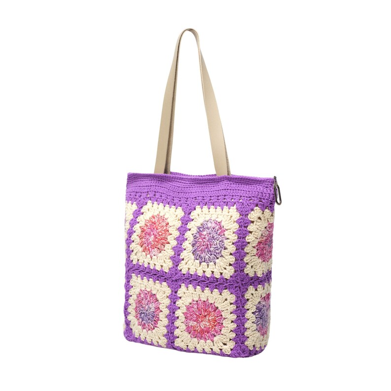 May include: A purple crochet tote bag with a cream-colored handle. The bag features a pattern of colorful squares in shades of pink, purple, and cream. The bag is designed with a zipper closure.