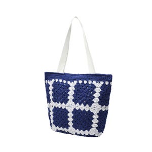May include: A blue and white crochet tote bag with white handles. The bag features a geometric pattern of white squares against a dark blue background. The handles are made of a smooth, white material.
