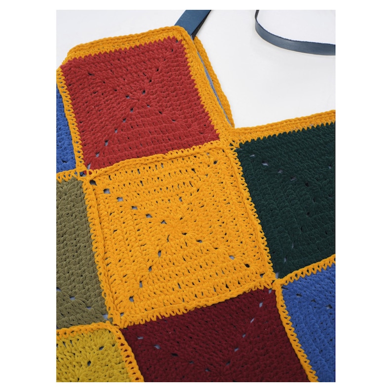 Puede incluir: Un bolso tote de crochet colorido con un dise&ntilde;o de patchwork. El bolso est&aacute; hecho de cuadrados en varios colores, incluyendo rojo, amarillo, verde y azul. Tiene una correa azul oscuro.