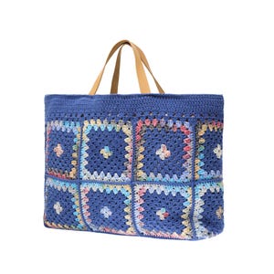 Puede incluir: Un bolso tote de crochet azul con un dise&ntilde;o de patchwork. La bolsa presenta una serie de cuadrados coloridos con detalles florales. Tiene asas de cuero marr&oacute;n y un interior espacioso, perfecto para llevar lo esencial.