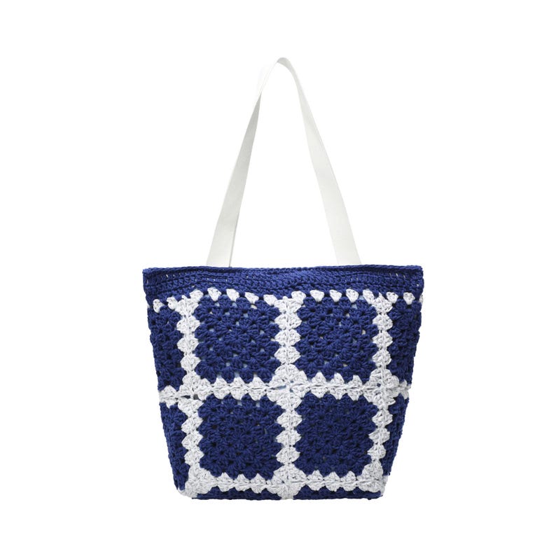 May include: A handmade tote bag with a crocheted design. The bag features a navy blue and white pattern, with white straps. The bag is made of yarn and is suitable for carrying items. The bag is a stylish accessory.