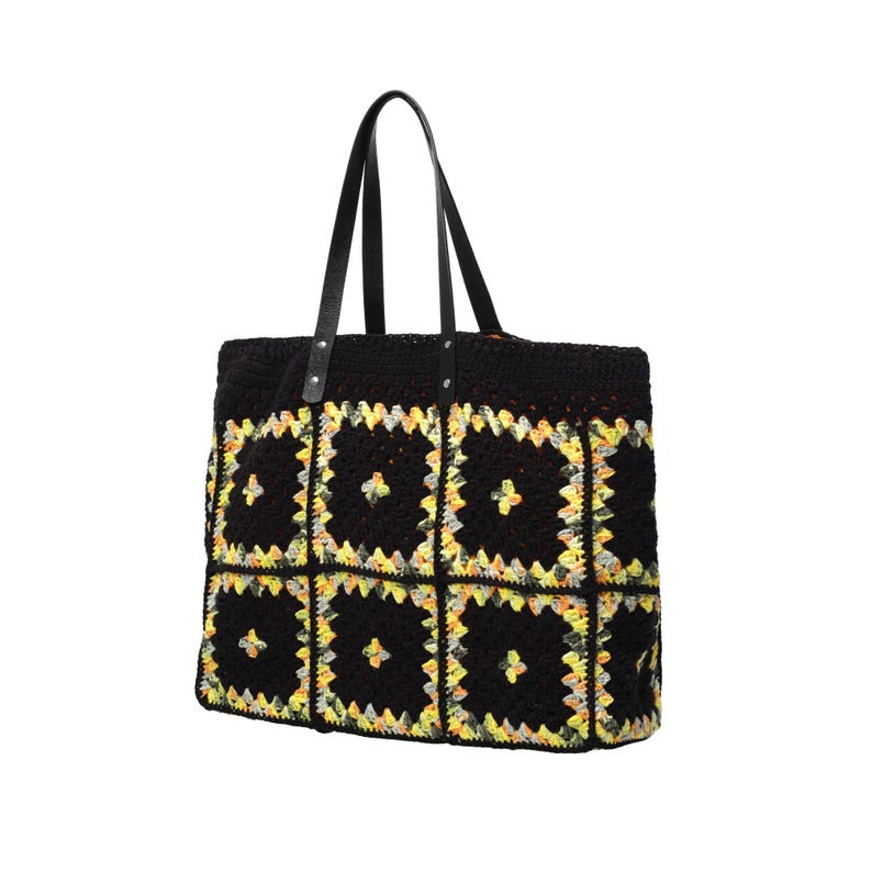 Puede incluir: Bolso tote de crochet negro con un dise&ntilde;o de patchwork con detalles en amarillo y naranja. El bolso tiene dos asas de cuero negro. Un accesorio elegante para llevar art&iacute;culos.
