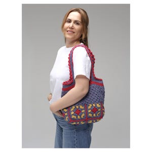 May include: A handmade crochet tote bag in shades of blue, red, and yellow. The bag features a granny square design with a scalloped red trim and handles. The bag is carried over the shoulder.