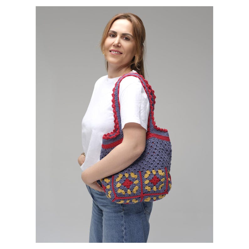 May include: A handmade crochet tote bag in shades of blue, red, and yellow. The bag features a granny square design with a scalloped red trim and handles. The bag is carried over the shoulder.