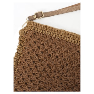 May include: A brown crochet bag featuring a detailed floral-inspired pattern with a textured surface. The bag includes a metallic gold-toned border along the top edge and a thin, adjustable brown strap attached with a gold-colored metal buckle.