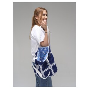 May include: A navy blue and white crochet tote bag with a white strap. The bag's interior is lined with blue fabric and white stars. The bag is carried over the shoulder.