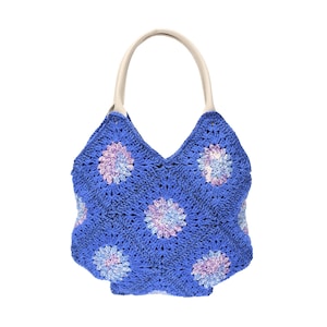May include: A blue crochet tote bag with a floral pattern in shades of purple and light blue. The bag has a cream-colored handle and a V-shaped top. The bag is made of a soft, textured material.