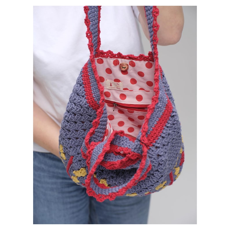May include: A handmade crochet bag in shades of blue, red, and yellow. The bag features a red polka dot lining and a red zipper. The straps and edges are trimmed with red crochet. The bag is held by a person wearing a white shirt and blue jeans.