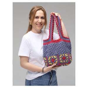 May include: A handmade crochet tote bag in shades of blue, red, and yellow. The bag features a granny square design on the front and a scalloped edge. The bag is held up by a person.