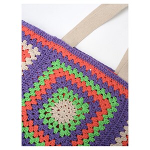 Puede incluir: Primer plano de un bolso tote de ganchillo colorido. El bolso presenta un vibrante patr&oacute;n de cuadrados de la abuela en tonos morado, naranja, verde y beige. El bolso tiene una correa beige y est&aacute; hecho de un material suave y texturizado.