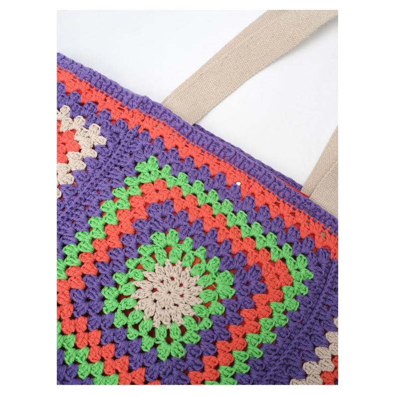 Puede incluir: Primer plano de un bolso tote de ganchillo colorido. El bolso presenta un vibrante patr&oacute;n de cuadrados de la abuela en tonos morado, naranja, verde y beige. El bolso tiene una correa beige y est&aacute; hecho de un material suave y texturizado.