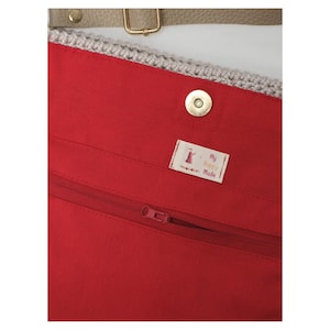 May include: A close-up of the interior of a red tote bag, featuring a zip, a magnetic clasp, and a label reading "My Happy Mode". The bag has a crocheted top edge and a tan strap with gold hardware.