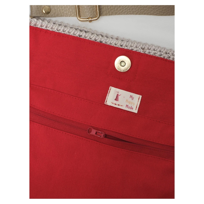 May include: A close-up of the interior of a red tote bag, featuring a zip, a magnetic clasp, and a label reading "My Happy Mode". The bag has a crocheted top edge and a tan strap with gold hardware.