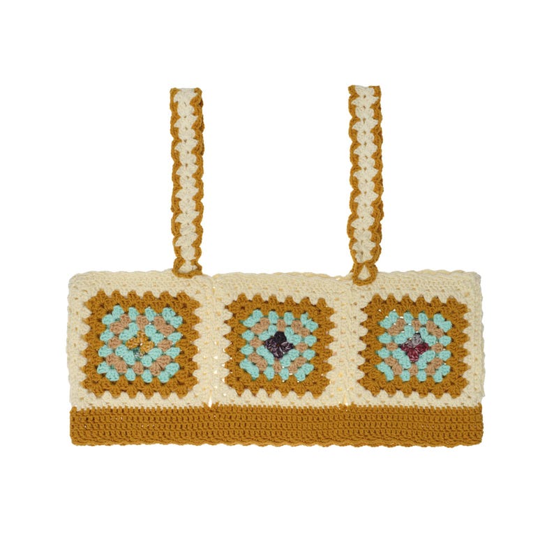 May include: A crochet crop top featuring three square granny motifs in cream, mustard yellow, and light blue. The garment has two wide shoulder straps and a solid mustard yellow band along the bottom edge, constructed with intricate yarn stitching.