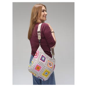 May include: A beige crochet shoulder bag with colourful square patterns. The bag has a cream-coloured strap and silver-tone hardware. The squares feature bright colours like pink, yellow, blue, and green. The bag is worn over the shoulder.