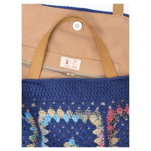 Puede incluir: Un bolso tote de crochet azul con un estampado floral colorido. El bolso tiene un asa de cuero marr&oacute;n claro y un interior marr&oacute;n claro. El bolso tiene un cierre de cremallera y un cierre de bot&oacute;n magn&eacute;tico. La etiqueta dentro del bolso dice "My Made".